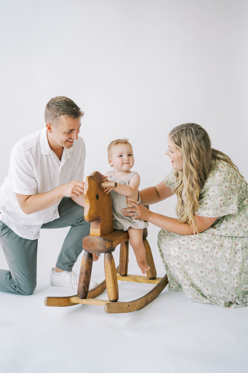 parents smiling at their baby while she plays on a rocking horse