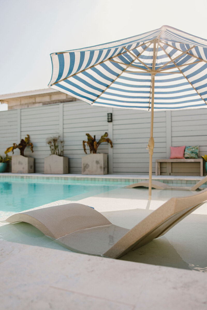pool lounger in water with striped umbrella