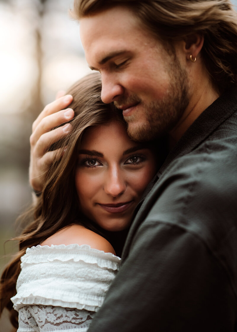 A woman grins at the camera while her man hold her close to his chest at Dawson Butte Open Space in Colorado. 