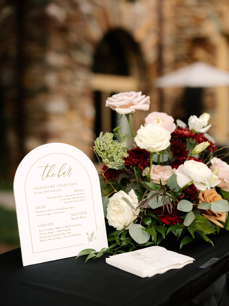 November wedding at Graylyn Estate, designed and planned by Charming Carolina — custom bar menu surrounded by blush and burgundy florals on the reception bar.