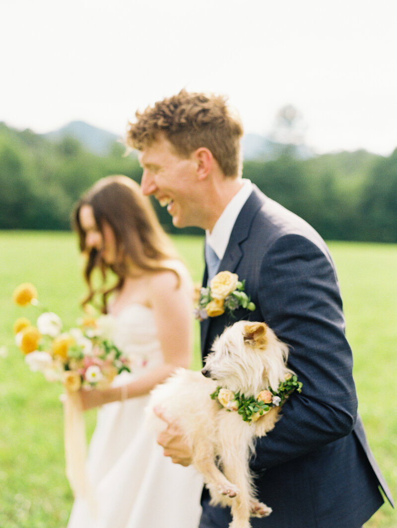 With a big smile, the groom carries their dog next to the bride after their destination wedding in North Carolina by film photographer Megan Lynn of My Sun and Stars Co.