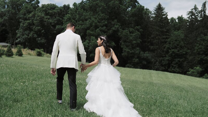Bride and Groom walk hand in hand up a field to overlook Keuka Lake at Crispin Hill wedding venue