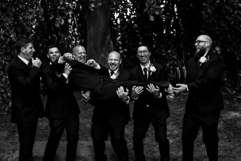 Groomsmen work together to lift laughing groom off the ground at the Schoolhouse in Fairview PA