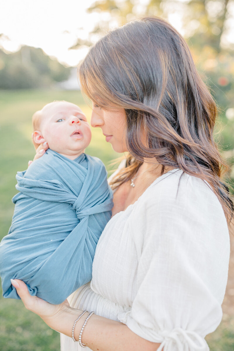 A loving mother cradles her wrapped newborn in her arms, gazing at him with pure adoration. Captured in soft, natural light, this intimate newborn session by a Fairfield photographer beautifully preserves the warmth and connection between mother and baby