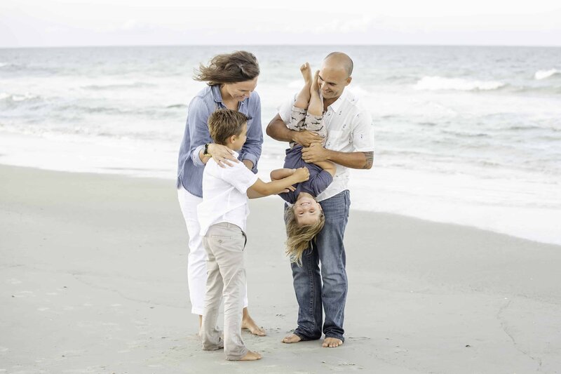Family on the beach having fun, dad holding kid upside down