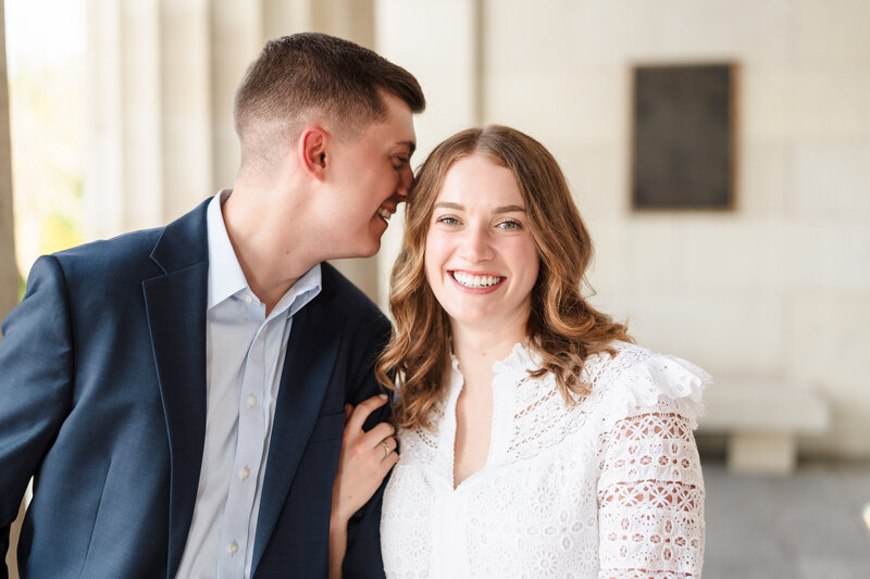 A young man in a blue sport coat whispers into the ear of his fiance during their Cincinnati engagement session