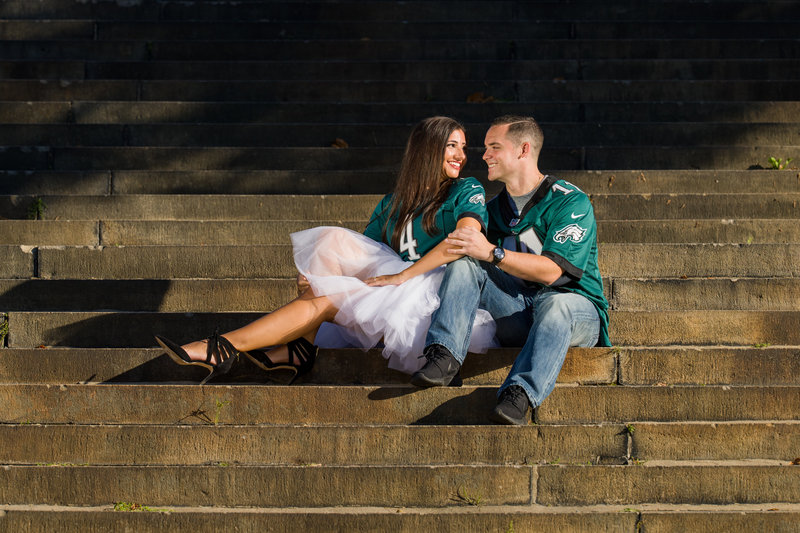 Couple dressed in Eagles attire sitting on the Philadelphia Museum of Art steps, combining team spirit with a Philly iconic spot.