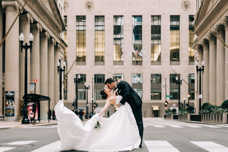 Extravagant Photo of Bride and Groom kissing on Chicago Street as groom dips bride and her long gown blows in the wind.