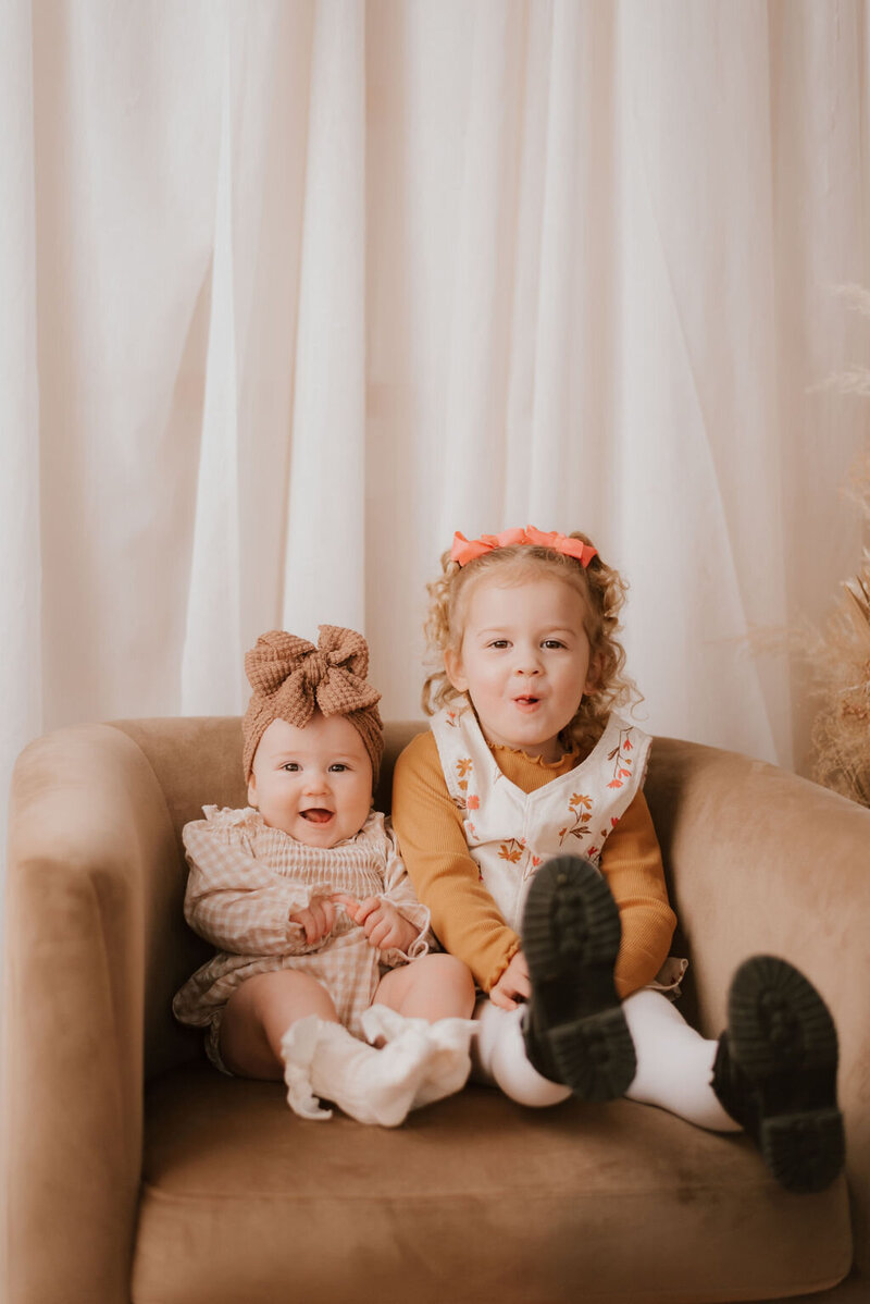 two sisters pose on chair for family photos in peoria illinois