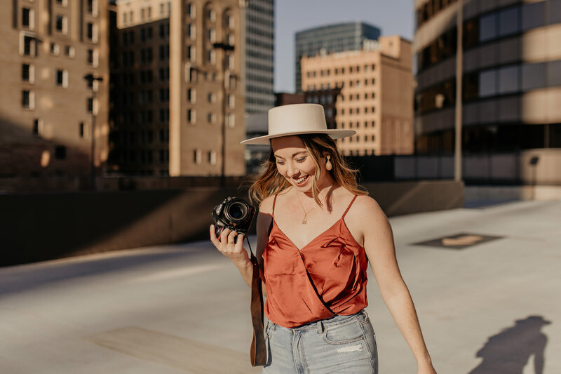 Photographer laughing and holding camera with tall buildings behind her.