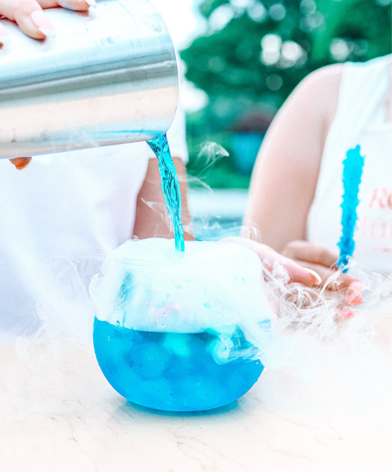 Blue cocktail being poured into a smoking candy fishbowl