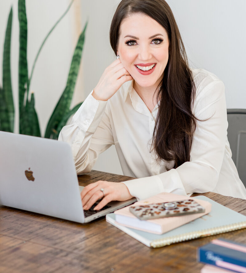 Ashley Turner, founder of Refresh Aesthetics sitting at a desk with her laptop