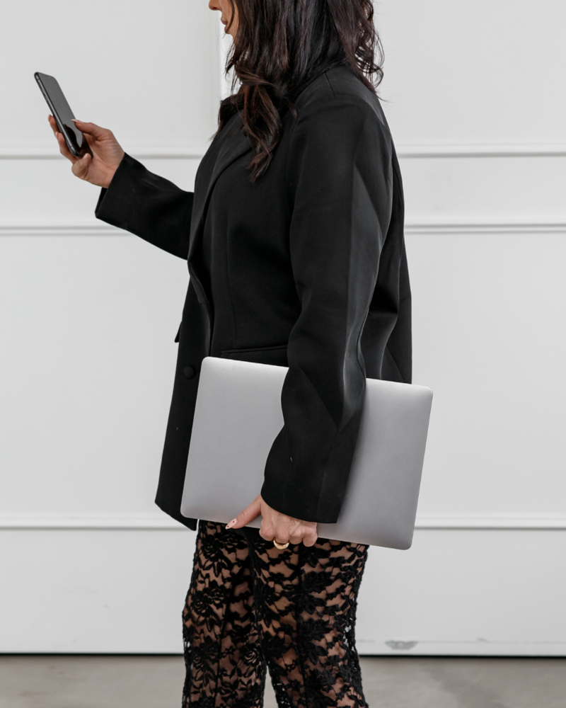 Woman holding a laptop looks at her phone