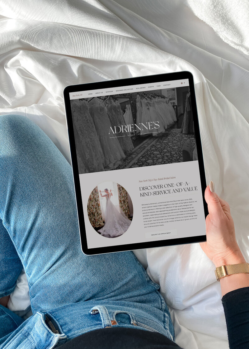 A hand holds an iPad displaying a brand website, with a cozy, casual setup in jeans—conveying calm, confidence, and the ease of viewing a beautifully designed site on the go.