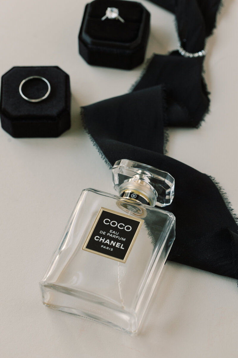 A chanel perfume bottle laying on black fabric with a velvet ring box.