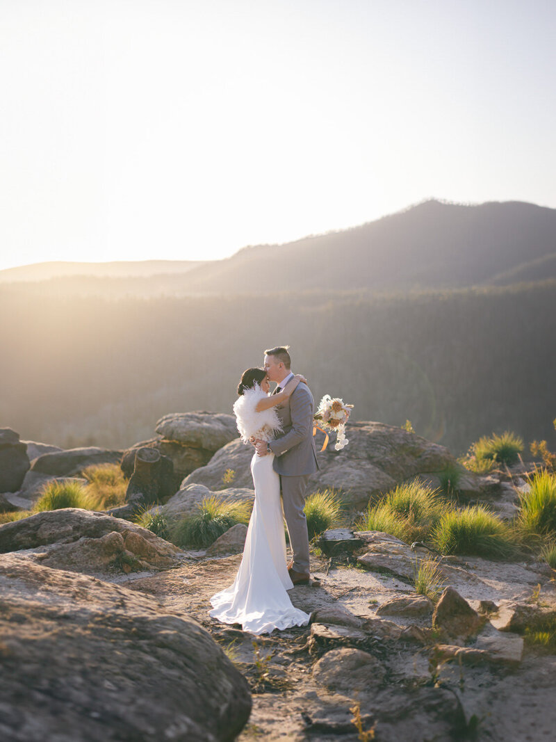 Bride and groom standing on cliff  in mountains at sunset on their wedding day