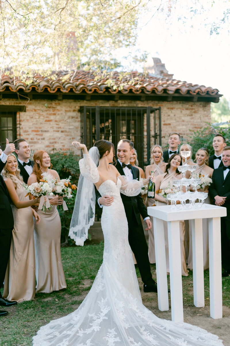 Groom pops a bottle of champagne to pour over champagne tower with his bride
