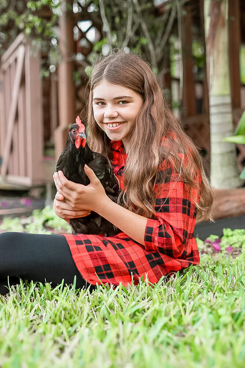 davie florida pet photography of a girl in a red flannel shirt holding her chicken while smiling at the camera