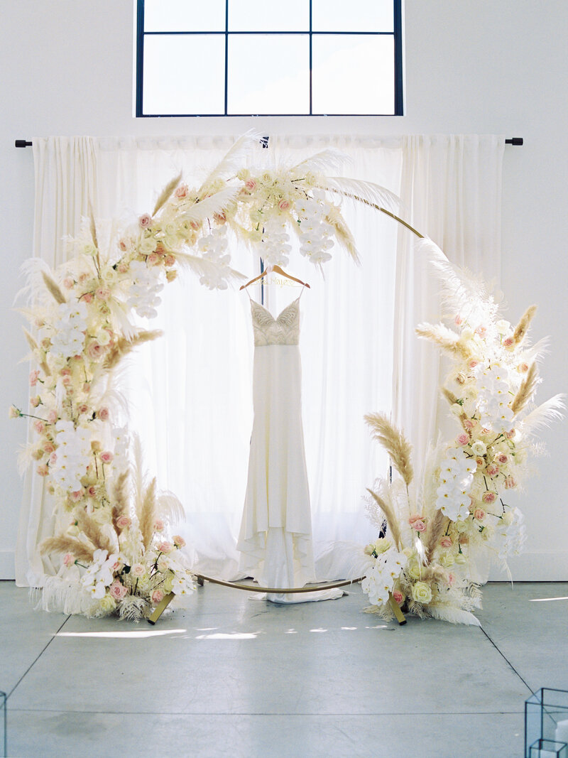 A brides wedding dress hangs beneath a floral boho arch at Barn South in Pednergrass, GA