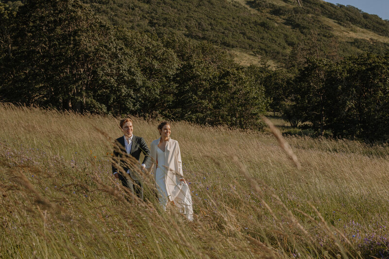 Bride and groom walking down grassy hillside