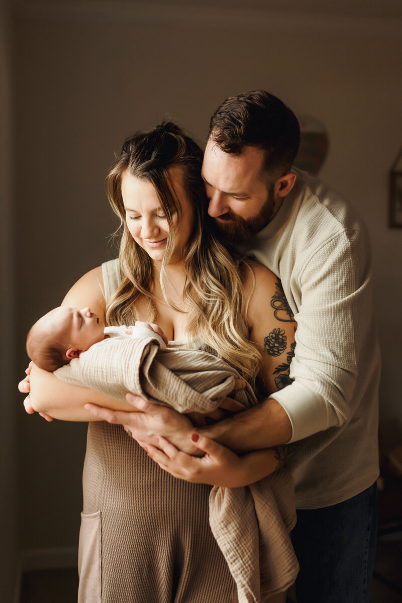 A couple snuggles and admires their newborn baby inside their home, photographed by a Vancouver Washington newborn photographer.
