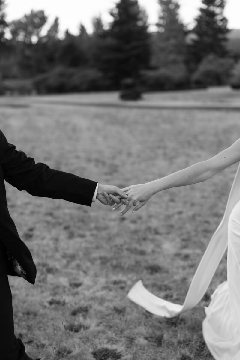 Bride and groom hold hands as they run through a field