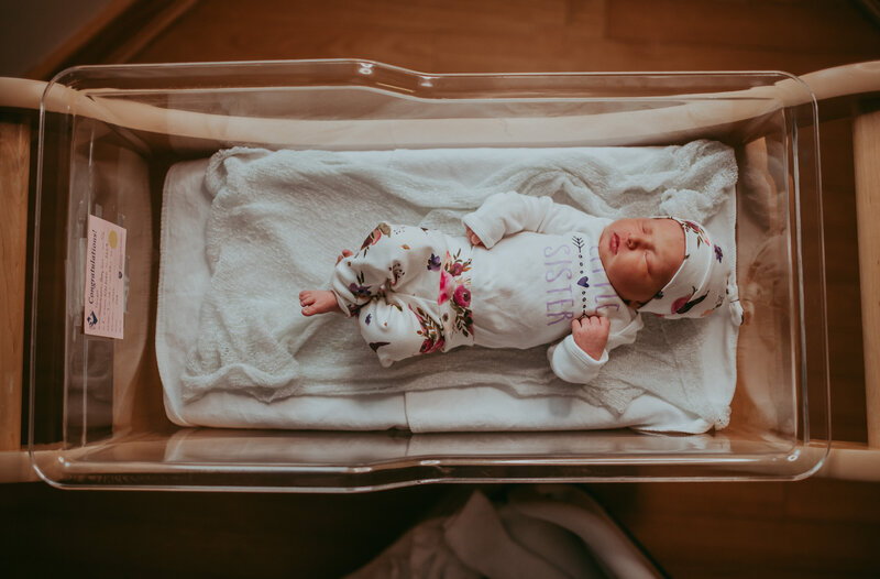 baby in the hospital laying in a bassinet with two boys and a woman