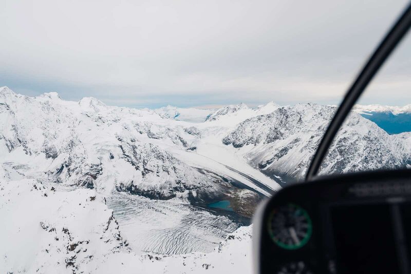 A sweeping view of the Knik Glacier ice falls taken from a helicopter on the way to an elopement vows ceremony on a the glacier during an Alaska Glacier Wedding.  with mountains, covered with snow, on the edge of the glacier valley.  