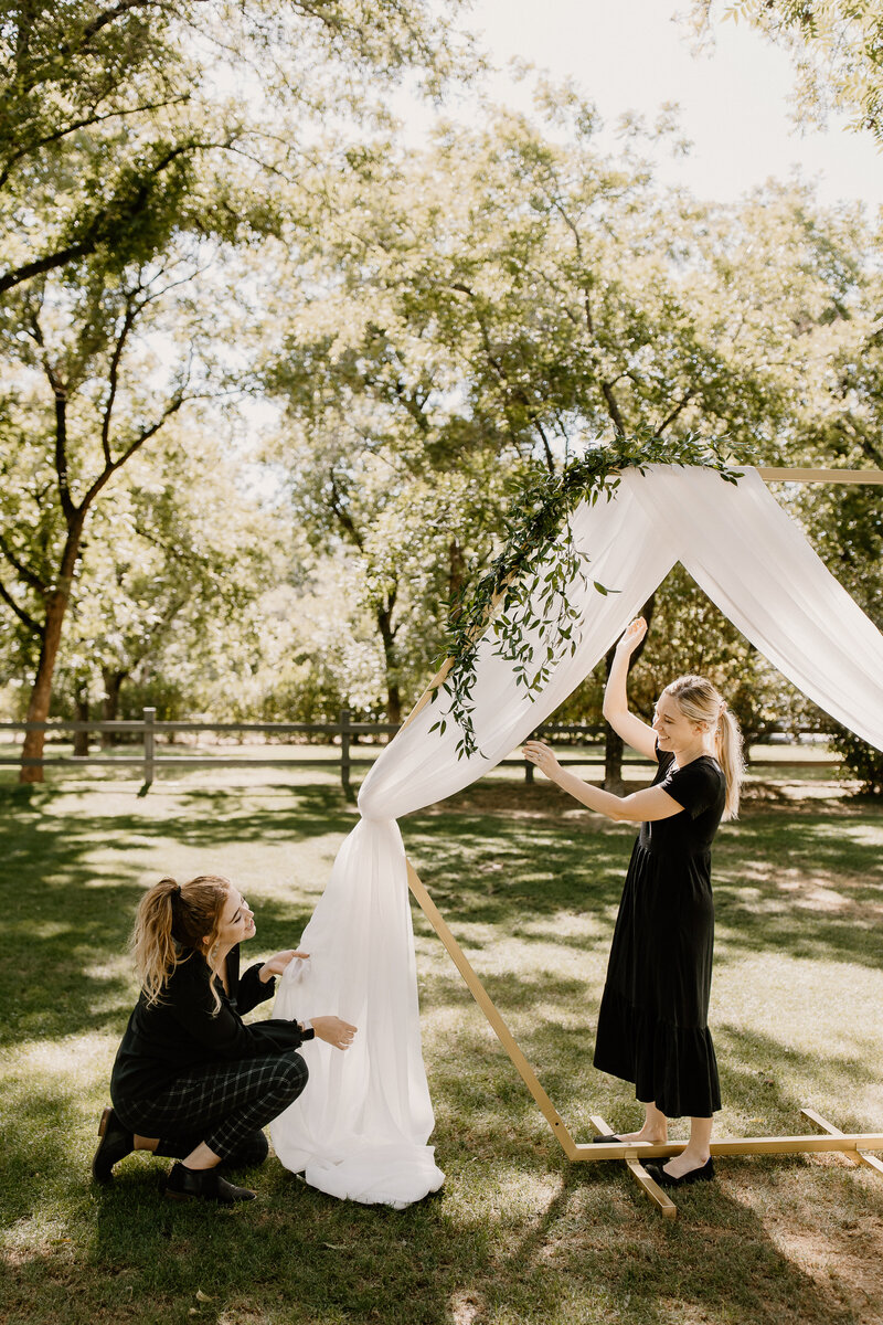 Shelby Helping Set-Up a Wedding Arbor with Draping and Greenery - Caitlin Audrey Photography
