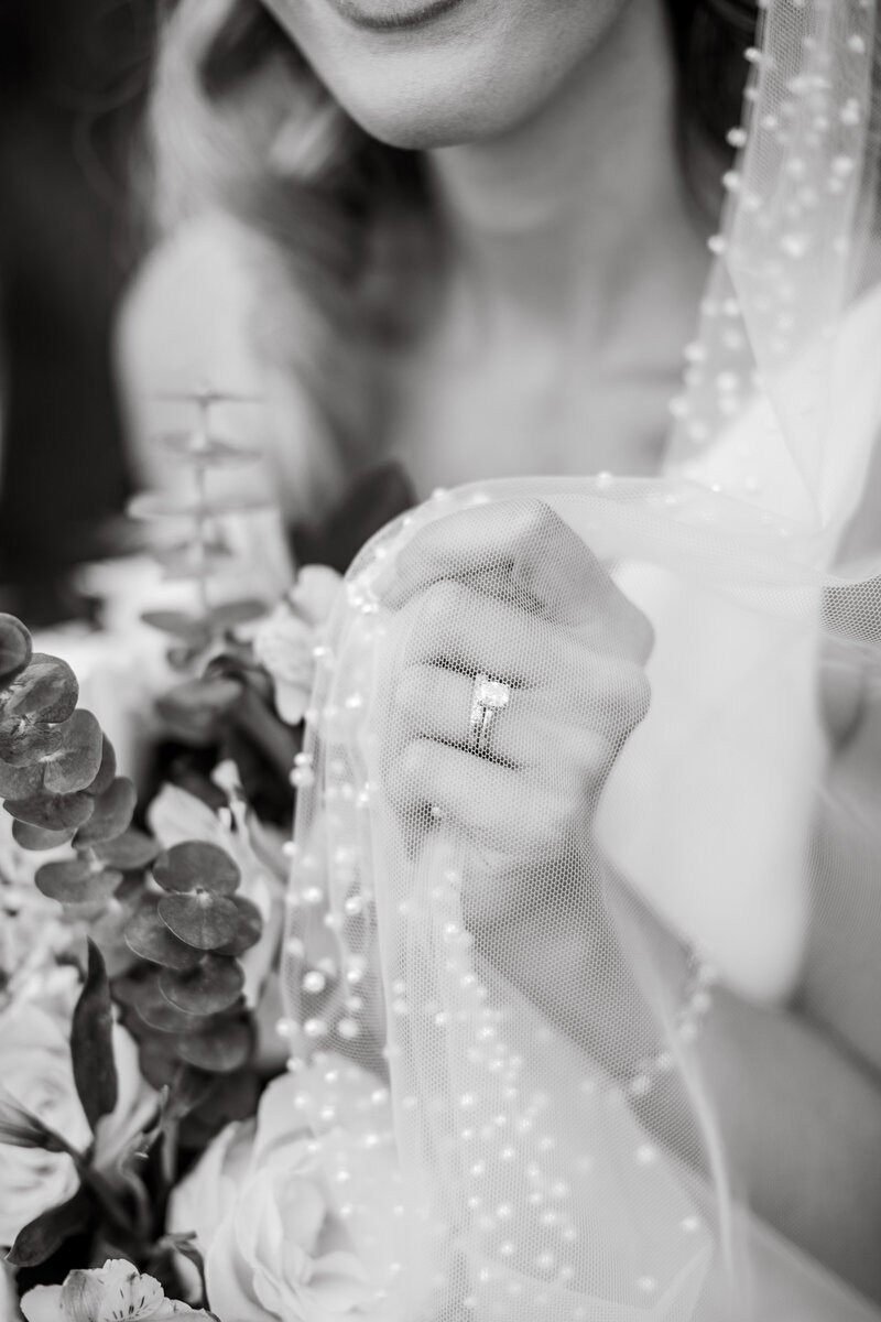 Black and white image of a brides hand grabbing her veil. The veil is lined with pearls