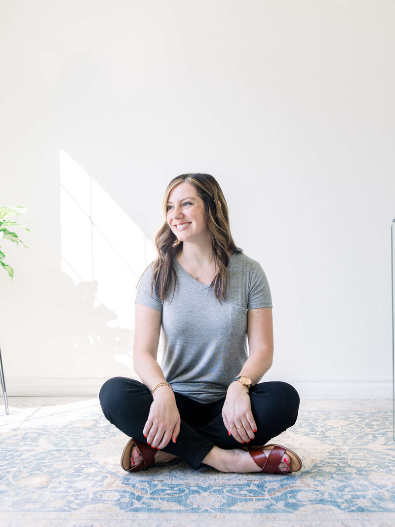 Woman in a gray t-shirt and black jeans sitting on the floor discussing website copywriting packages