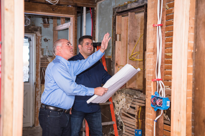 Two men holding a blueprint and talking about the house under renovation in Teaneck, New Jersey