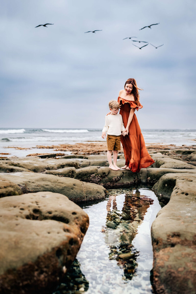 A mother and son stand together looking down at the Windansea tide pools in San Diego, California