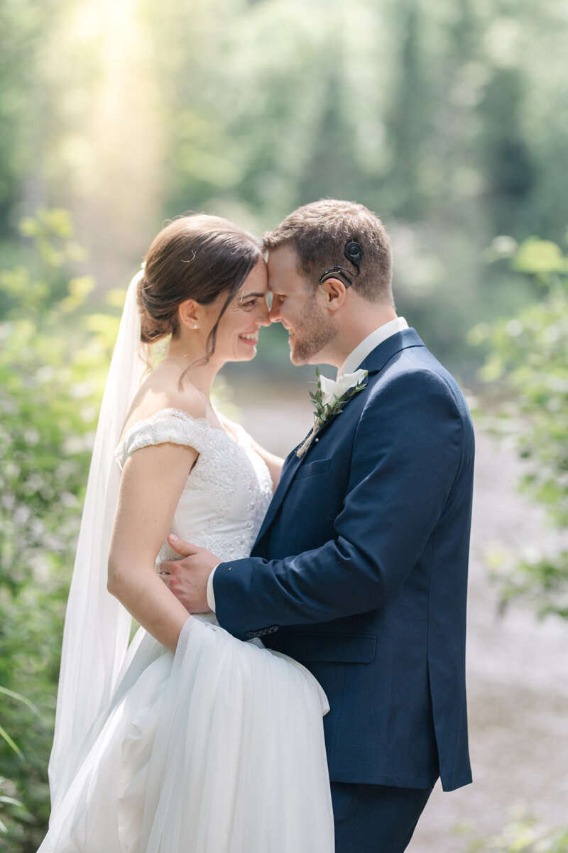 Les mariés, tendrement enlacés, partagent un moment intime et complice au bord d’un cours d’eau dans les Laurentides, scène naturelle et apaisante d’un mariage au charme authentique