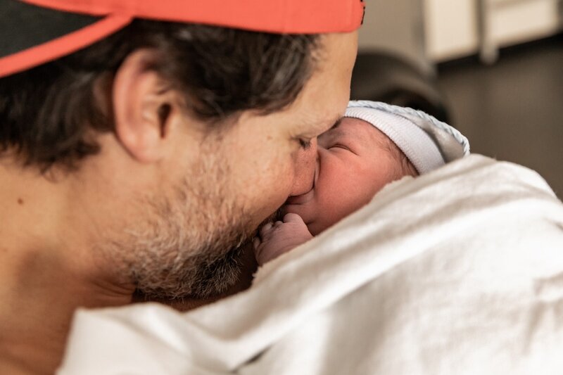 Een pasgeboren baby zuigt op de neus van haar vader.