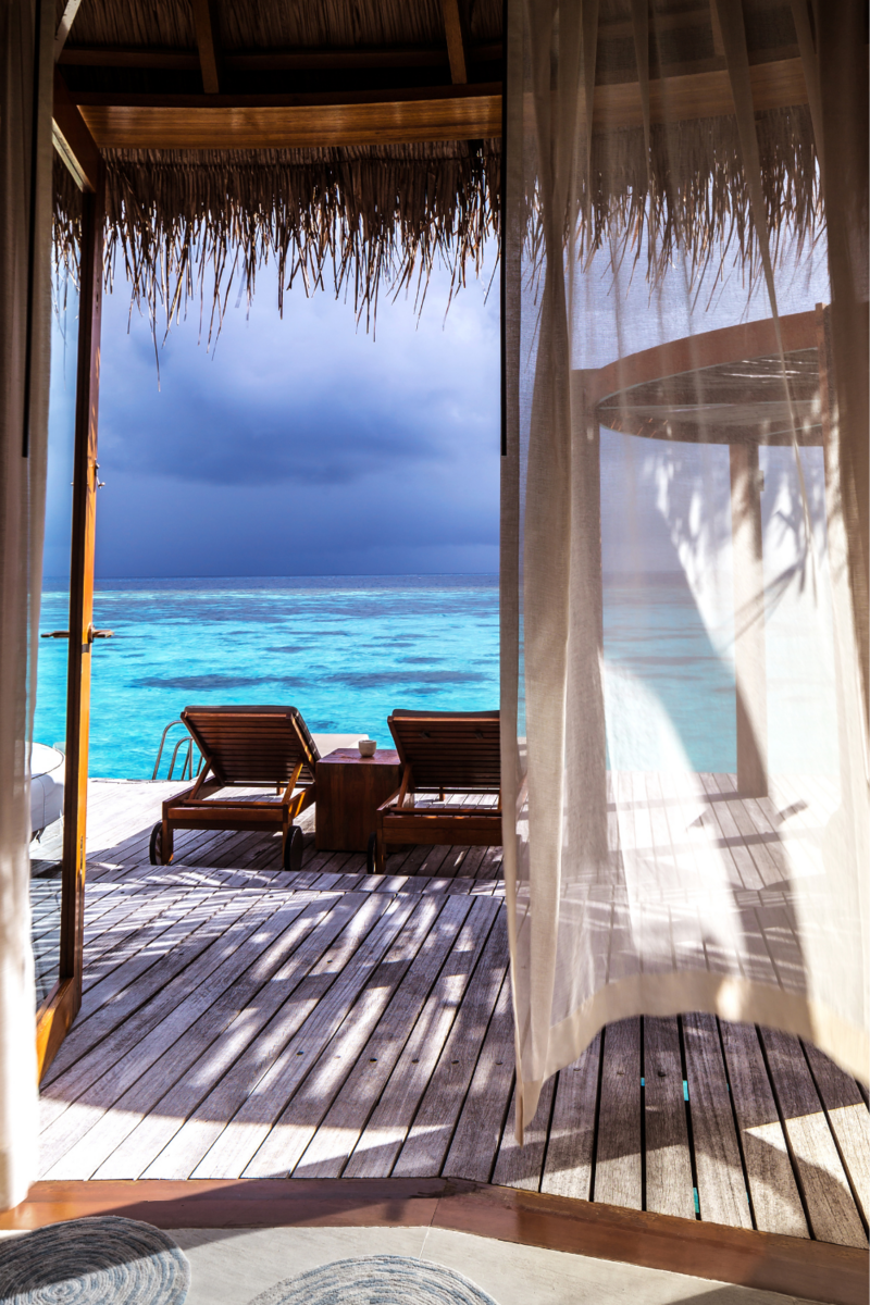 Two lounge chairs on deck overlooking blue water behind sheer curtain