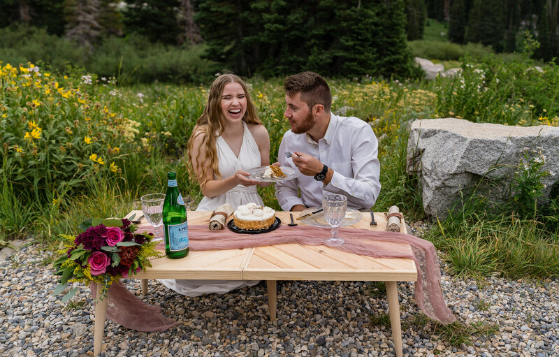 Bride and groom laughing with each other surrounded by the mountains near Salt Lake City, Utah having a picnic just the two of them to celebrate their elopement.