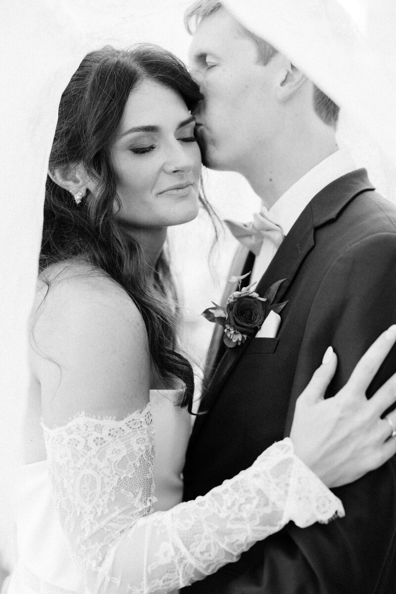Closeup black and white photo of a groom kissing his bride's cheek