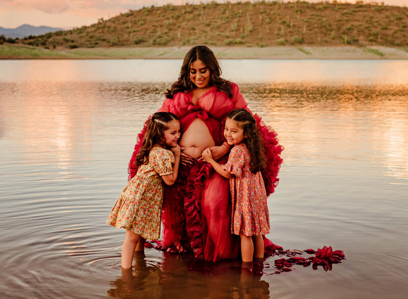 arizona mom with two daughters hugging her maternity belly in lake pleasant for photography session