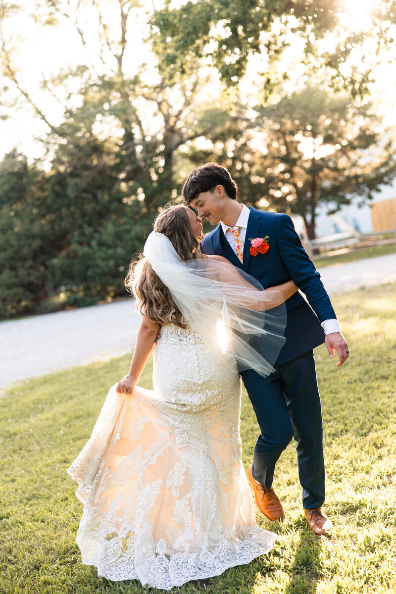 Bride and groom with noses touching and veil swooping across frame in golden light after Wichita wedding ceremony