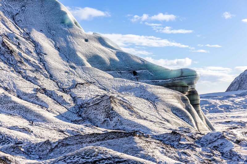 A bride and groom are embracing standing at a mountain overlook. They just says "I do" and are sharing a smile before their first kiss. The groom is holding the brides waist and the bride is holding the grooms face. The groom is wearing an olive green suit and the bride is in a long white lace dress.