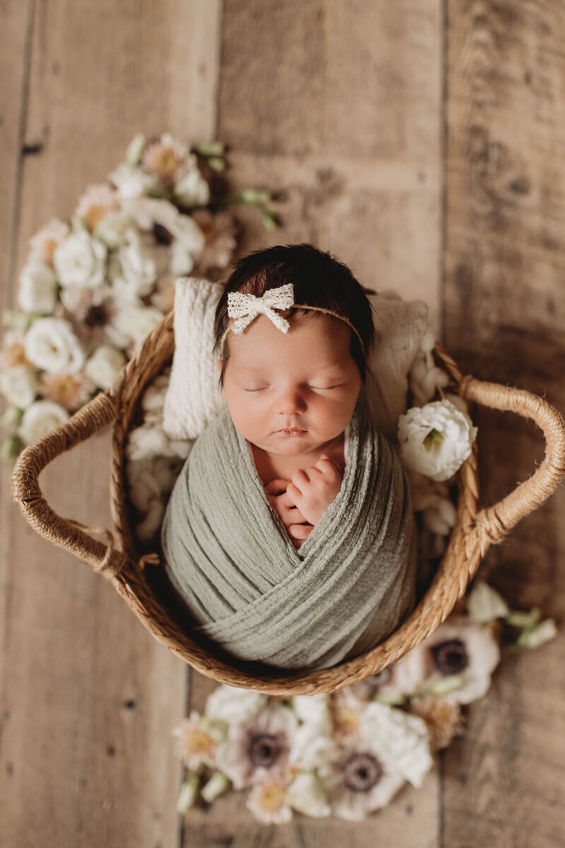newborn girl wrapped in a sage green blanket and placed in a wooden basket