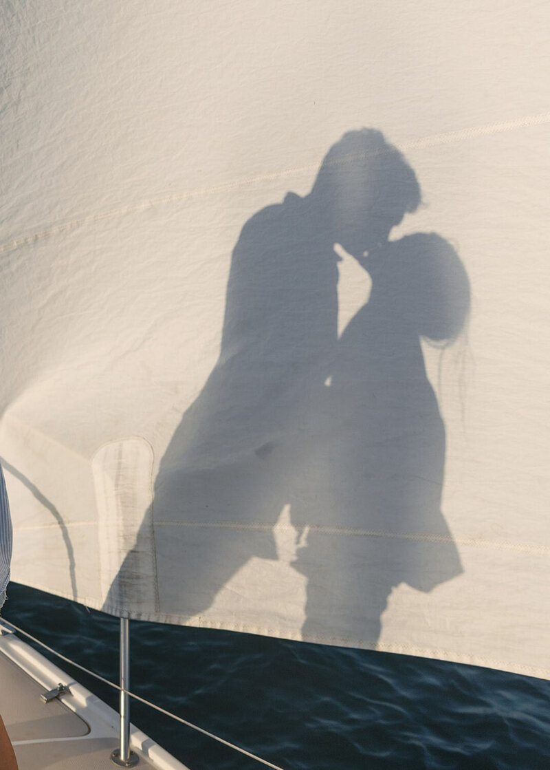 Silhouettes of two people kissing are cast onto a sailboat's sail,