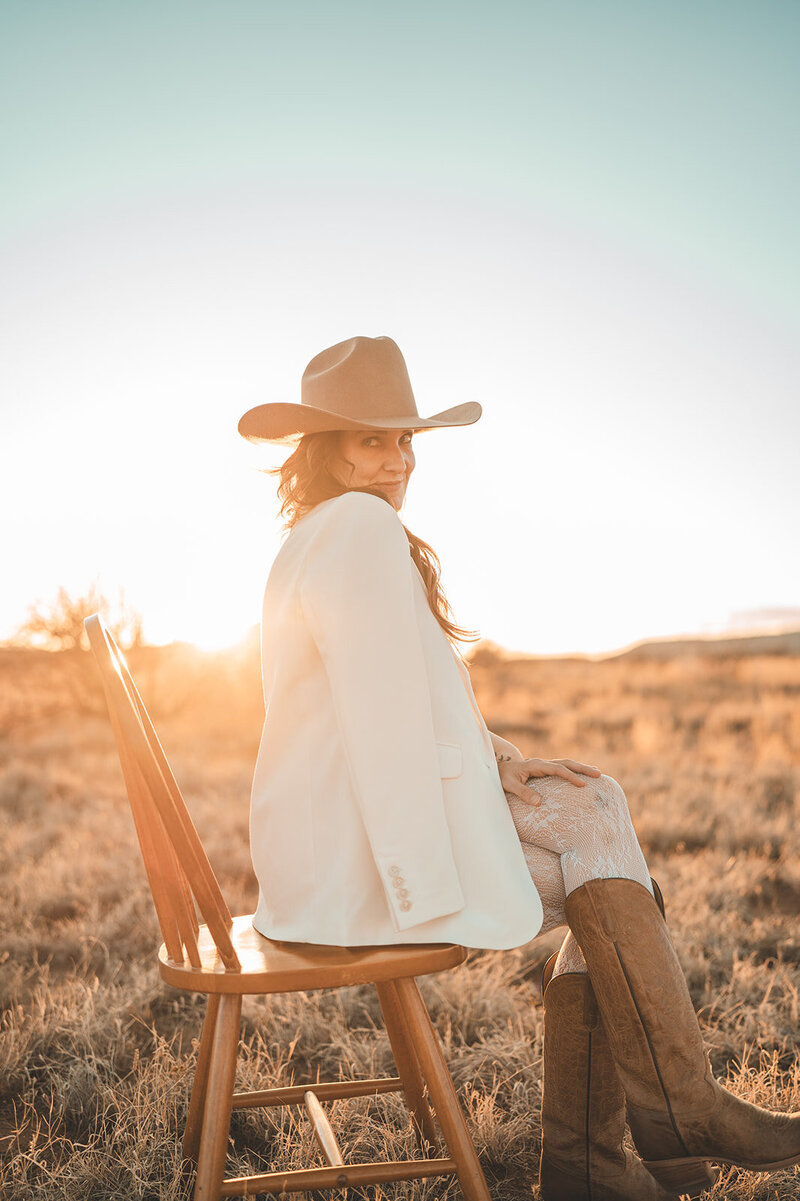 Outdoor brand portrait of Juliet Trnka wearing a brown cowboy hat and light beige blazer, sitting on a chair-part of the Direct Knowing brand photos