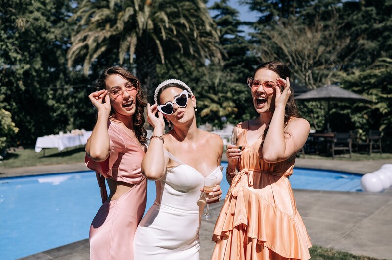 bridesmaids in pink and peach blak dresses with bride in trish peng dress beside the pool on a sunny day