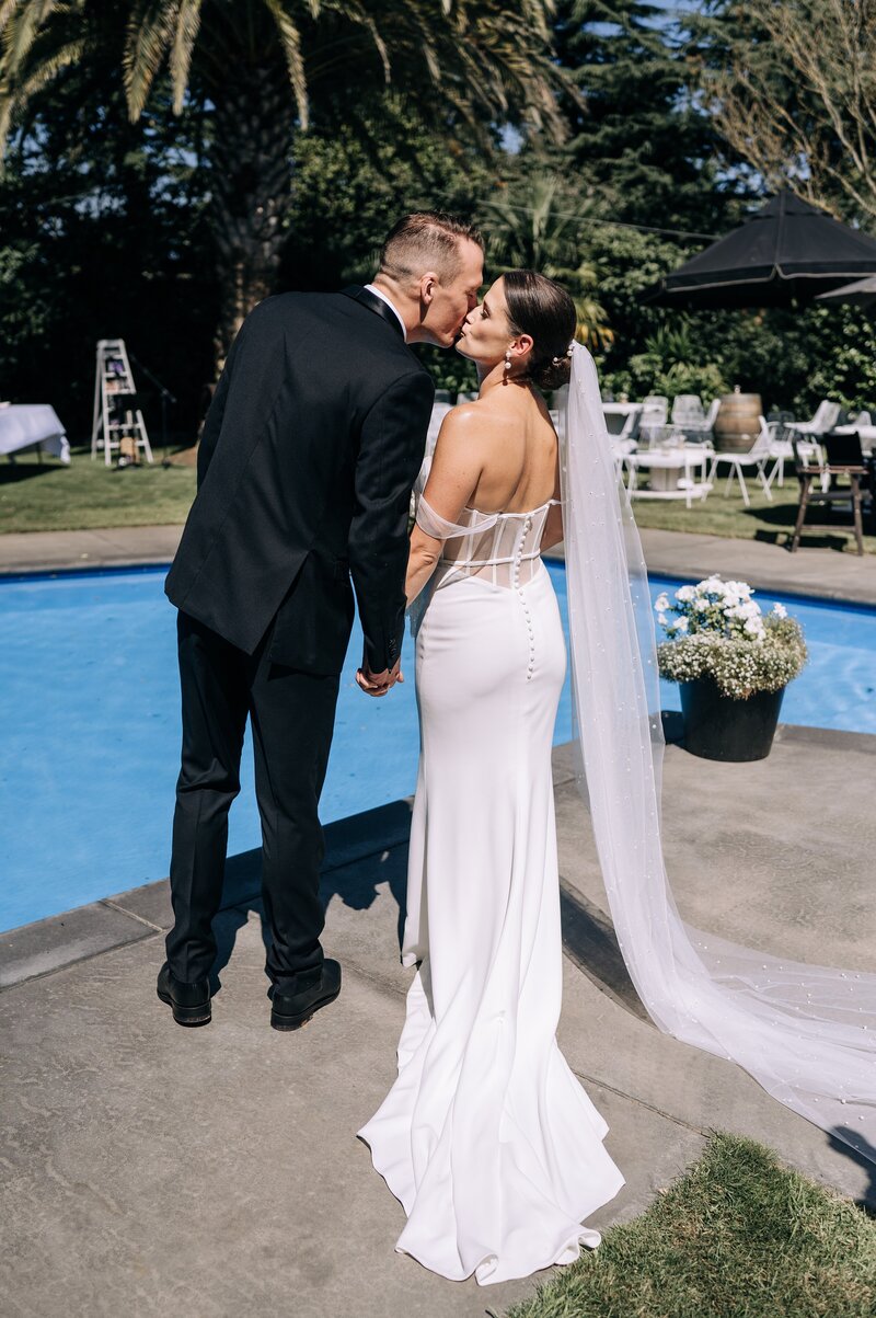 bride in trish peng dress kisses groom beside the pool in her backyard wedding in christchurch