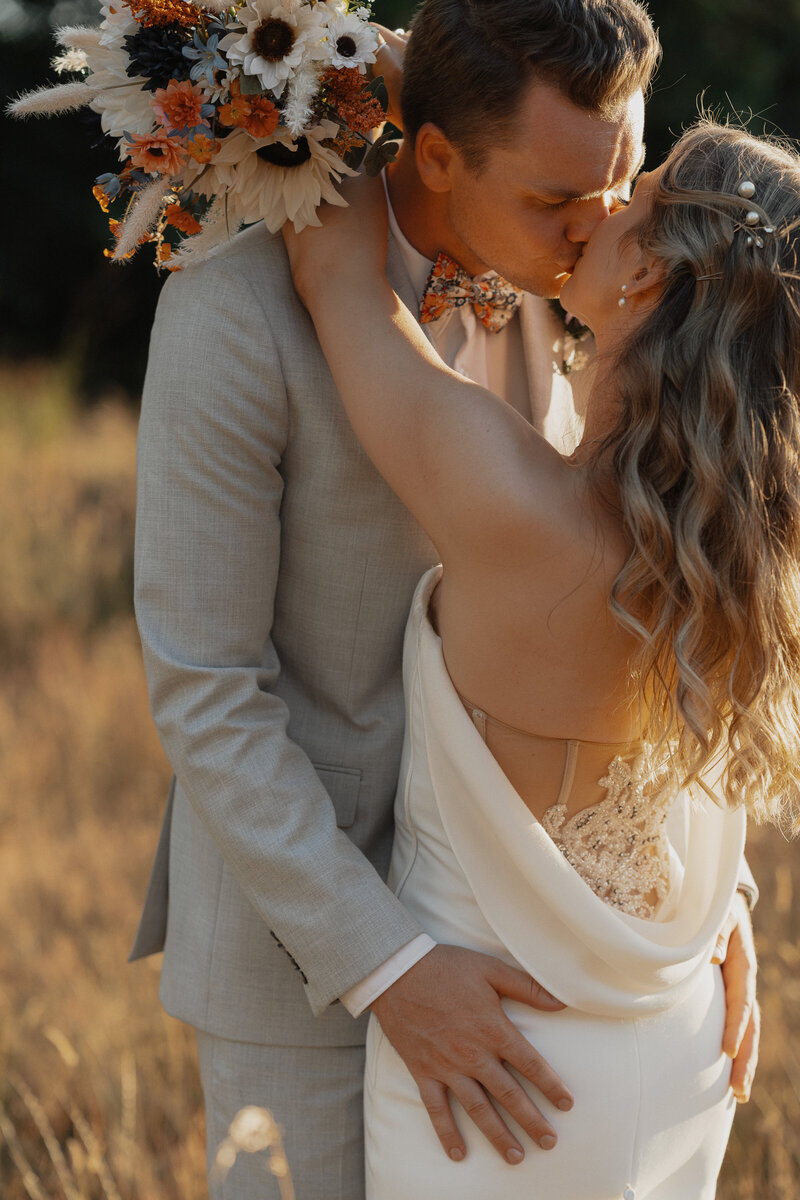 Bride and groom kissing in a field of tall grasses during their golden hour wedding portraits in comox by latitude 49 photography