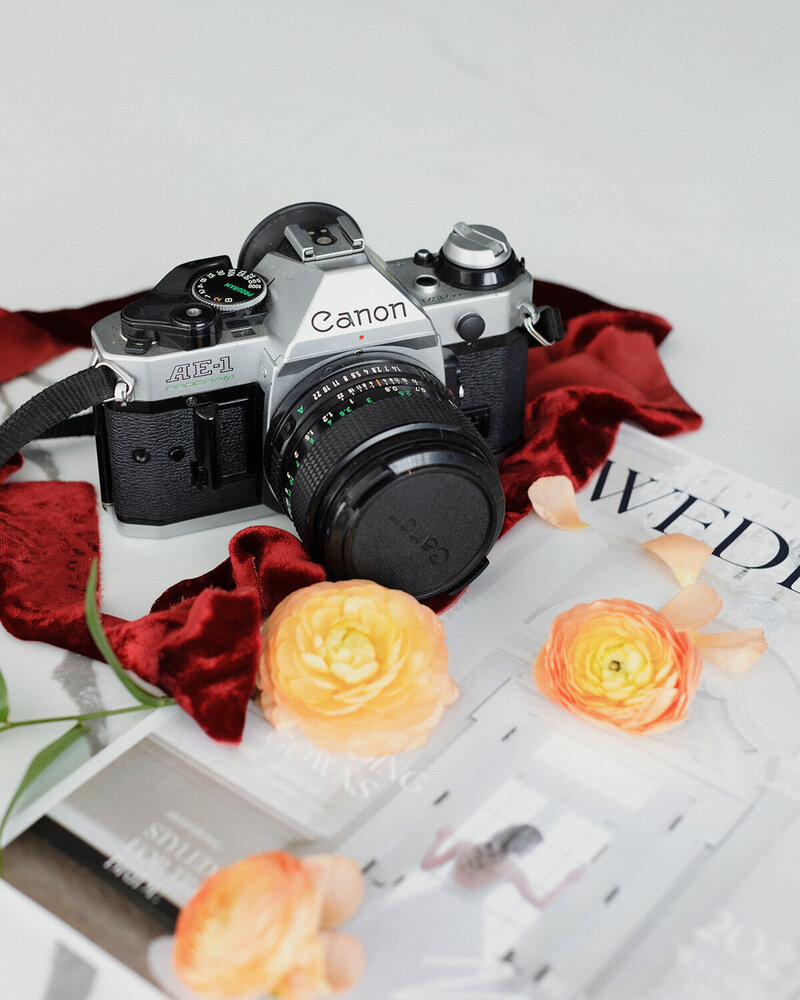 A photo of a Canon camera with a red elegant cloth and flowers surrounding it