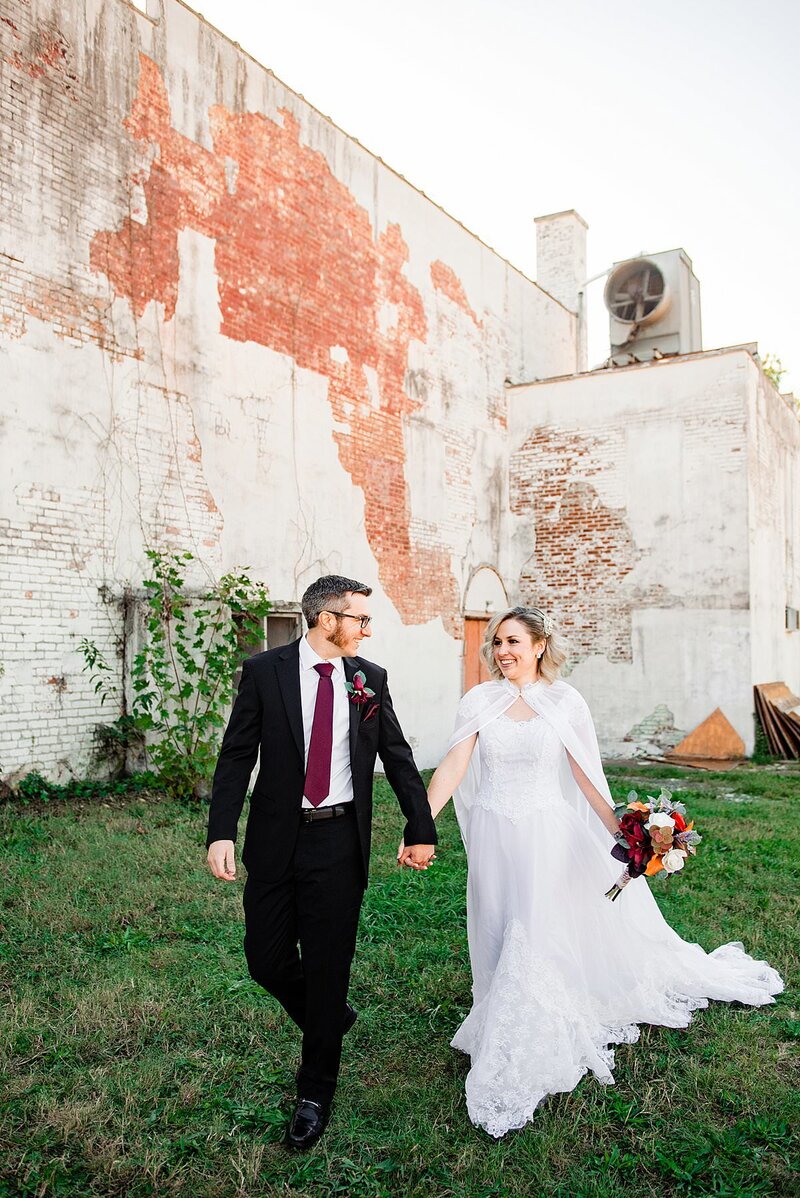 Couple holding hands and walking near Wilburn Street Studio in Nashville, they are smiling at one another and wearing their wedding outfits
