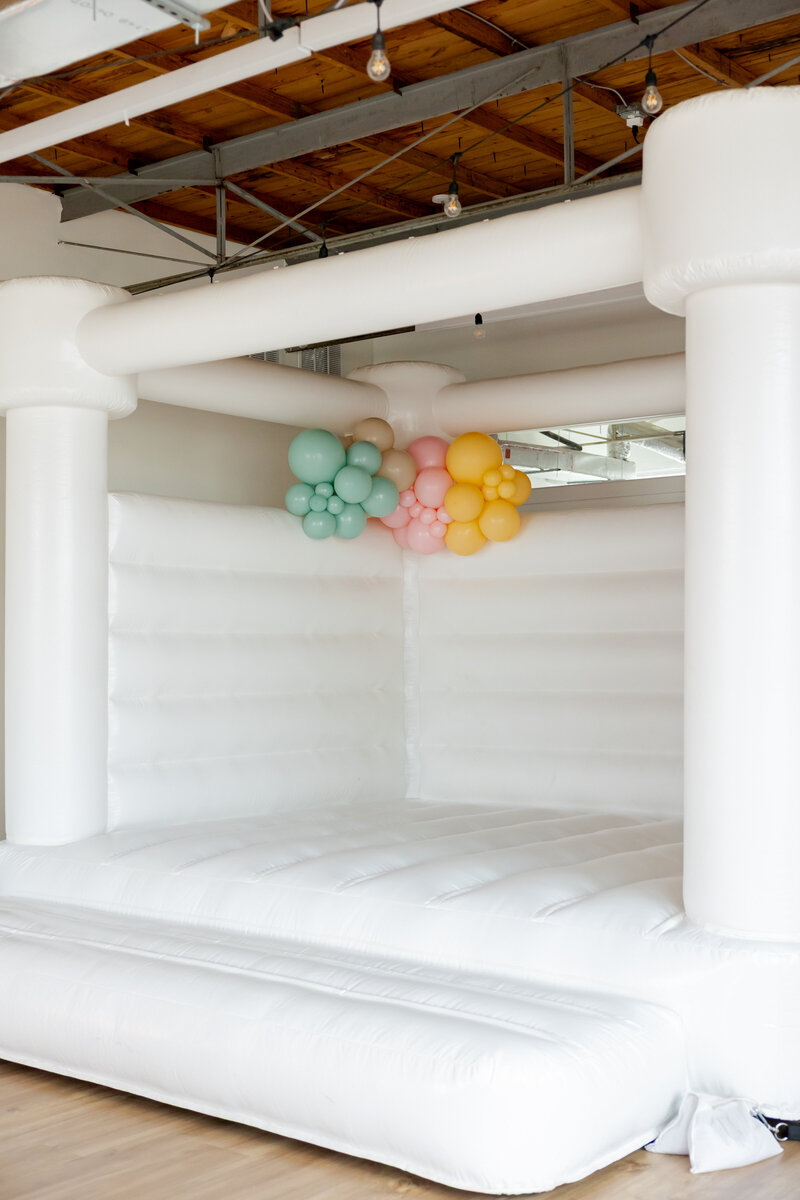 Small yellow, mint, and pink balloons on a white bounce house.